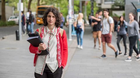 Woman standing, staring straight at camera wearing a backpack and carrying books.