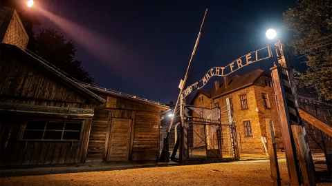An image showns a night time view of Auschwitz I: Main Gate. From the exhibition "Auschwitz. Now.” Image: © Copyright 2019 Perry Trotter