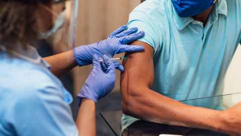 The image shows a man in a facemask being vaccinated by a female health worker: Pacific and Māori people must be prioritised for Covid-19 vaccination. Photo: iStock