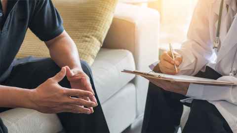 The image shows a male talking to a medical practitioner - the faces of both are not included in the photo.