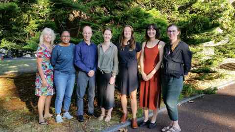 Photo of the full SDS team as of the start of 2020. The team is standing in front of a green bush.