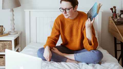 student sitting on bed looking at laptop