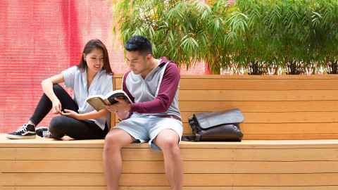 Students reading a book while sitting on a bench outside