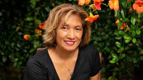 Dr ’Ema Wolfgramm-Foliaki in front of some bright orange hibiscus.