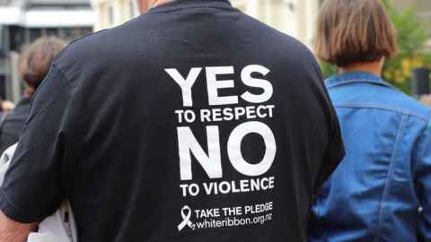 The image shows a man in a No to Violence t-shirt by the White Ribbon organisation: One in three New Zealand women has experienced physical, sexual or coercive violence from an intimate partner in her lifetime. Photo: Lynn Grieveson, Newsroom