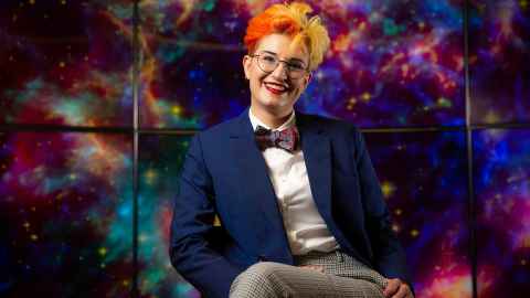Dr Heloise Stevance is an astrophysicist in the Faculty of Science. She has colourful hair and is sitting in front of an image of her favourite supernova.