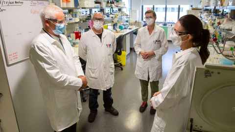 John Fraser explains vaccine to PM Jacinda Ardern in a lab, watched by Staph research team.