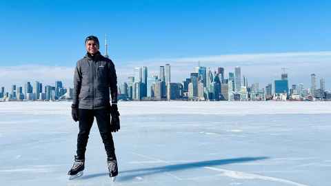 Mark Barboza ice skating on a frozen lake, with Toronto in the background.