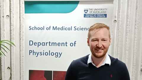 Dr Christopher Lear in front of Department of Physiology banner.