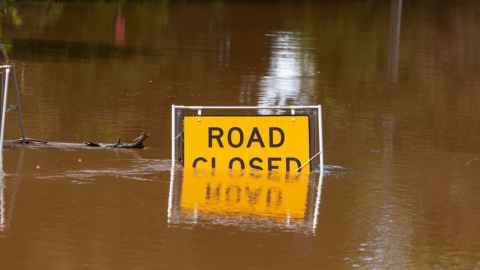 Road closed sign submerged in muddy water 