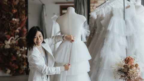 Katie Yeung in her design studio holding a wedding dress and smiling at the camera