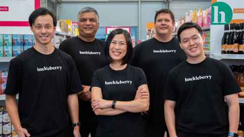 Five people standing in a row in the middle of a supermarket wearing black t shirts that say Huckleberry on the front