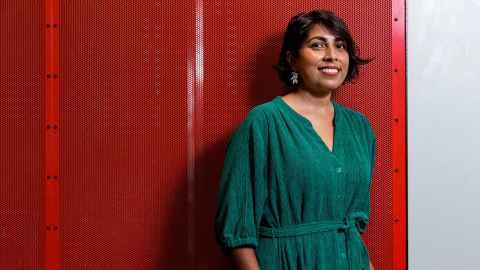 Dr Priyanka Dhopade wears green and stands in front of a red background. 
