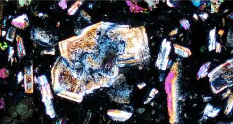 Light shining through a slice of glassy volcanic rock brings out the colours of the microscopic crystals within. 