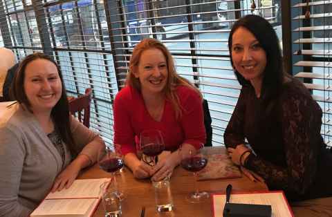 Three women sit smiling around a restaurant table.