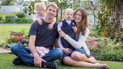 Rochelle Ade, her husband and their two young children sit on grass.