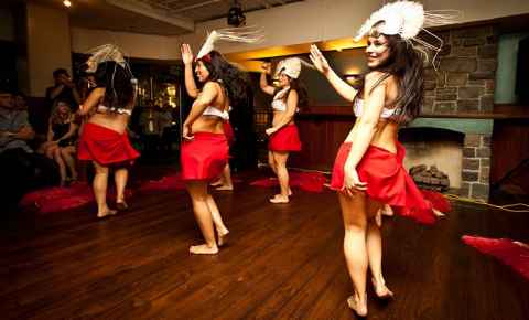 A group of four girls in Polynesian outfits - red skirts and white headresses - dancing.