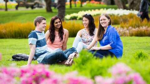Four students sit relaxed and smiling on the grass.