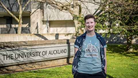 Ruth Monk outside the FMHS building next to a University of Auckland sign.