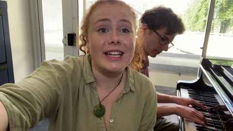 Student takes a selfie in front of another student playing the piano